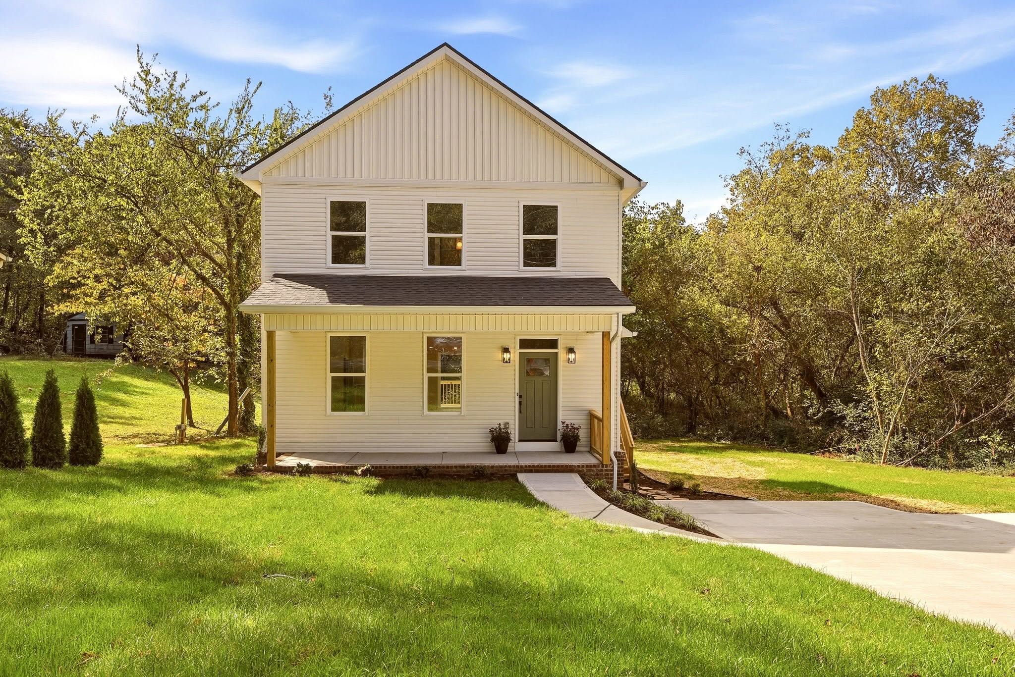 The finished Dewine Road house, straight on: board-and-batten gable, covered porch, and sage green front door