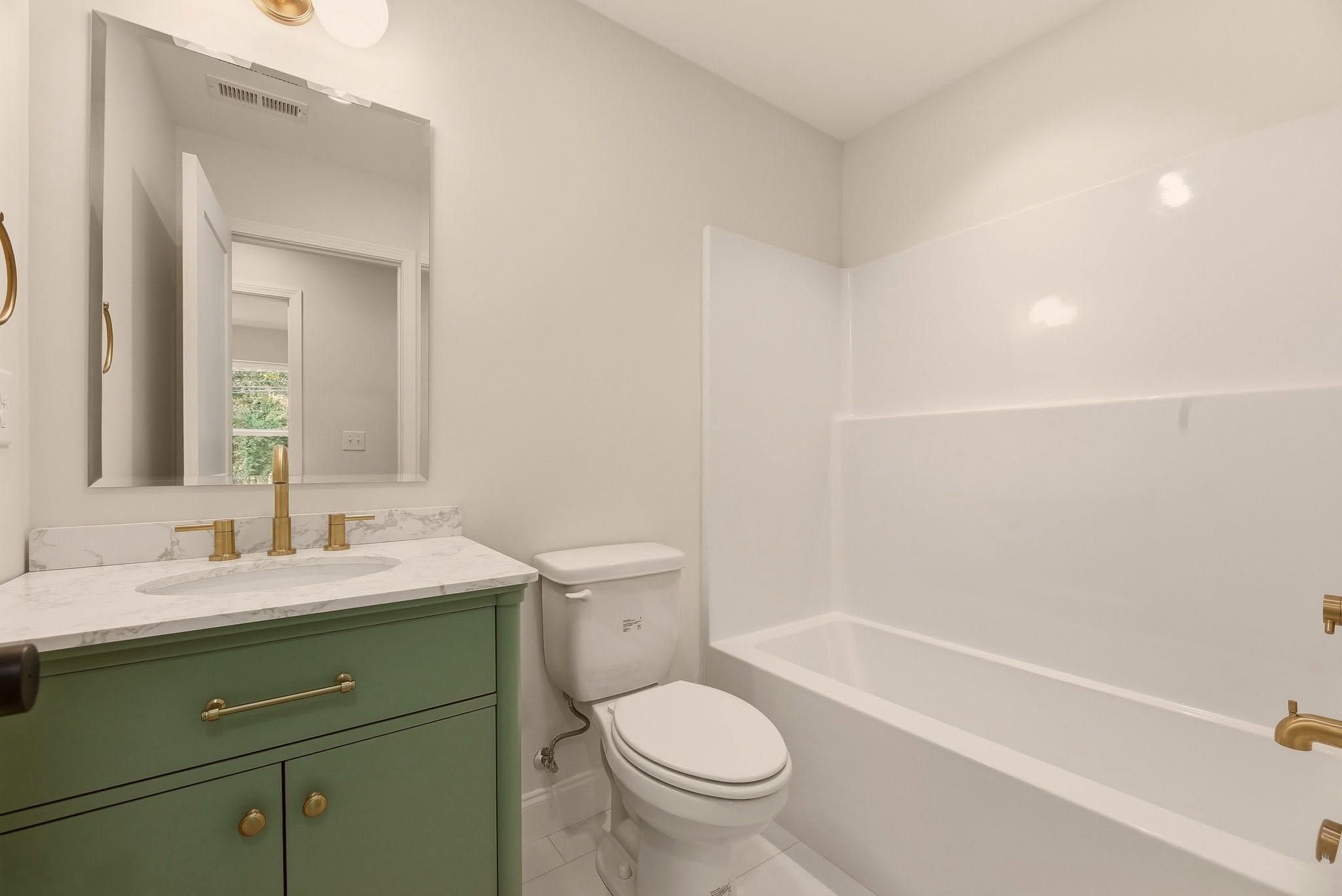 Finished hall bath with the sage green vanity, brass hardware, and white tub surround