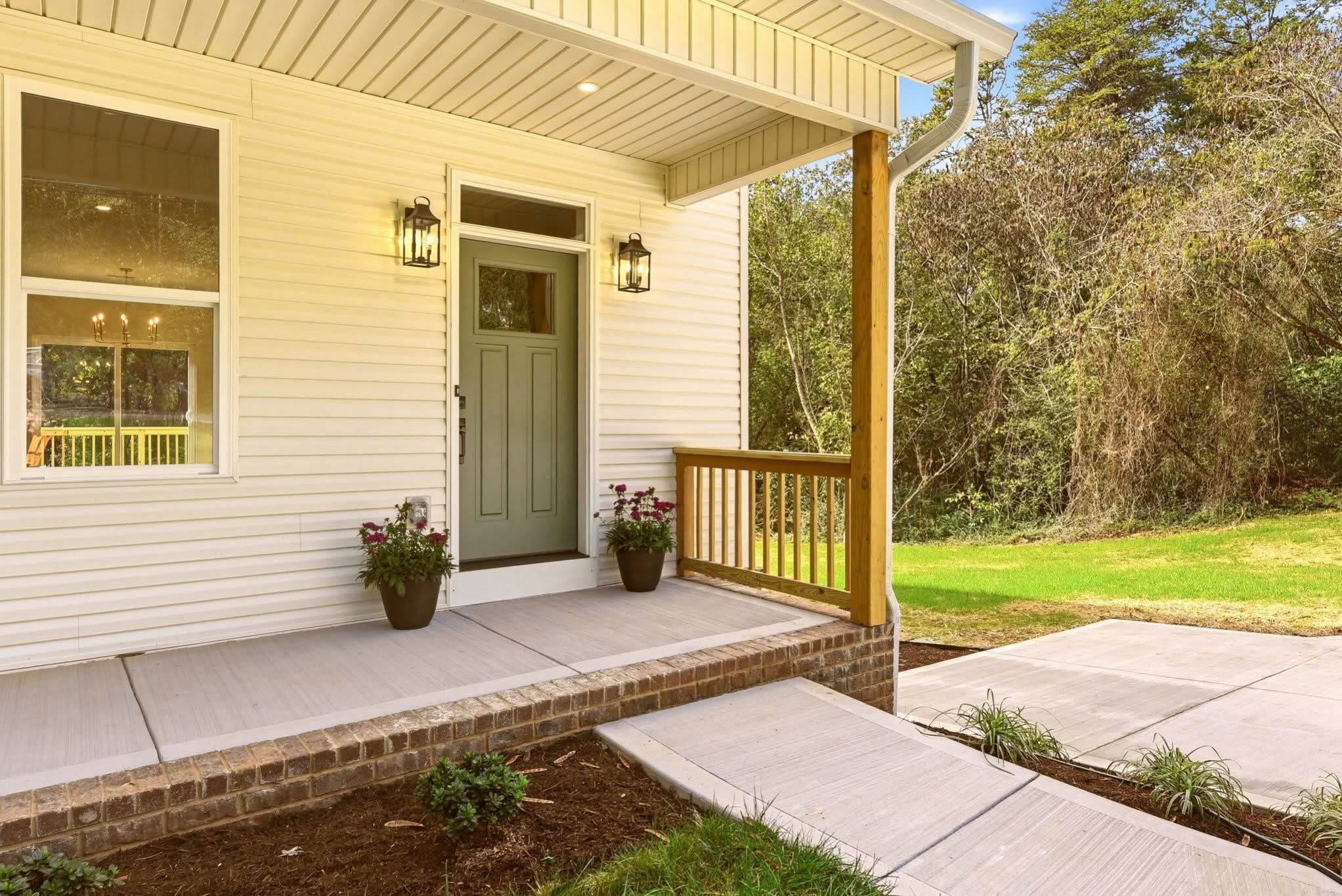 Covered front porch with a sage green craftsman door and black lantern sconces