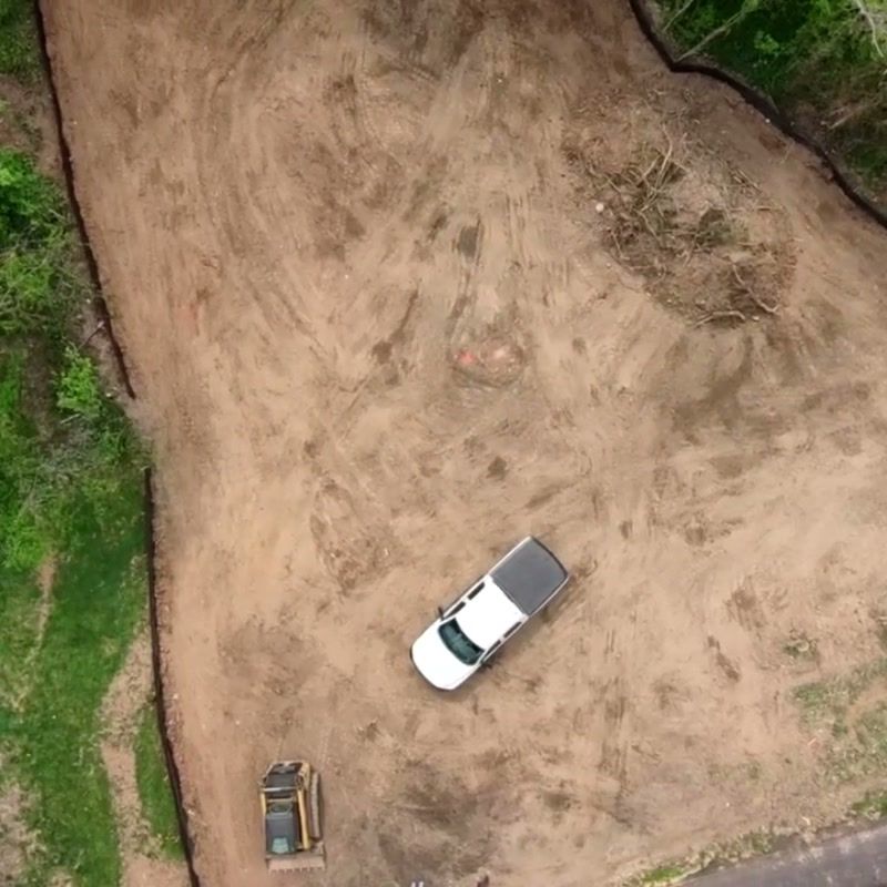 Aerial view of a cleared and graded lot with a pickup truck parked on the pad